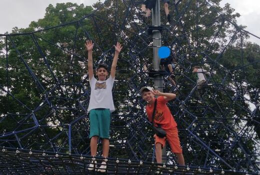 SchülerInnen klettern im Kletternetz. Im Vordergrund stehen zwei Jungs und lachen in die Kamera.