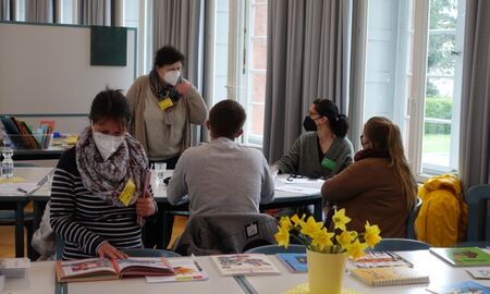 Besucher sitzen an Tischen, unterhalten sich oder sichten Materialien