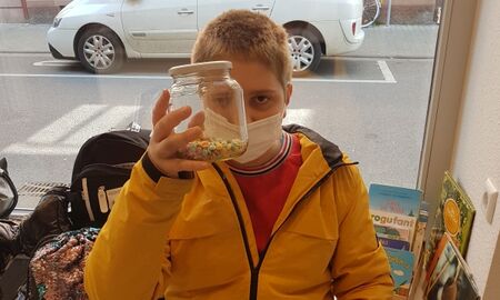 Ein Schüler sitzt am Fenster und hält ein Glas hoch, dass zu einem Fünftel mit Süßigkeiten gefüllt ist.