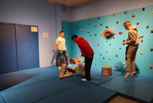 Zeit für Bewegung! Vier Schüler toben in einem Raum, ausgelegt mit Matten. An der Seite eine Boulderwand.