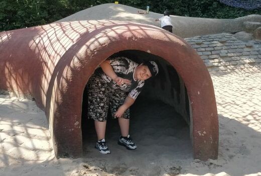 Ein Junge steht gebeugt am Eingang einer niederen Röhre. Er macht das Victory-Zeichen.