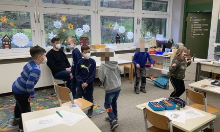 Fünf Zweitklässler und eine Zweitklässlerin tanzen im Klassenzimmer, während der Musiklehrer am Rand sitzt und zuschaut.