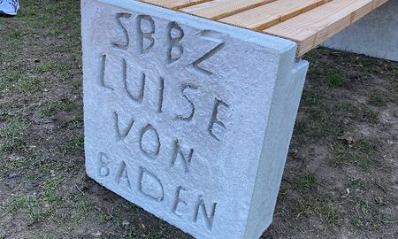 Eine Holzbank mit Seitenteil aus Beton. Darauf steht SBBZ Luise von Baden