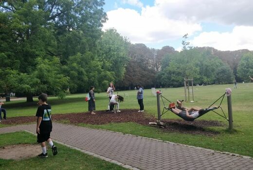 Blick auf eine Wiese mit spielenden Kindern. Zwei chillen in einer Hängematte.