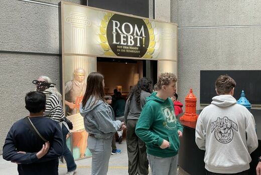 Sieben Personen laufen durch Ausstellungsräume mit Exponaten