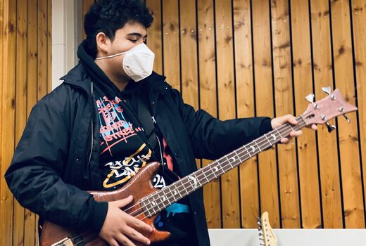 Ein Schüler steht mit Bass Gitarre umgehängt und spielt auf der Gitarre